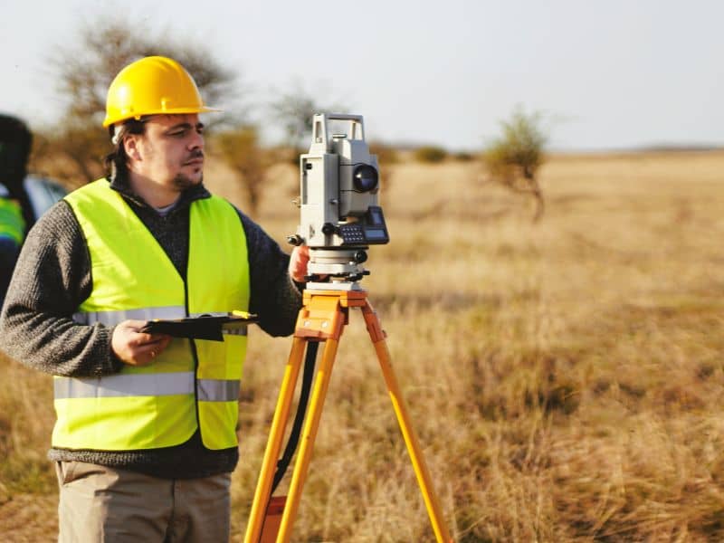 Land surveying professional using a total station to establish accurate property boundaries before residential improvements